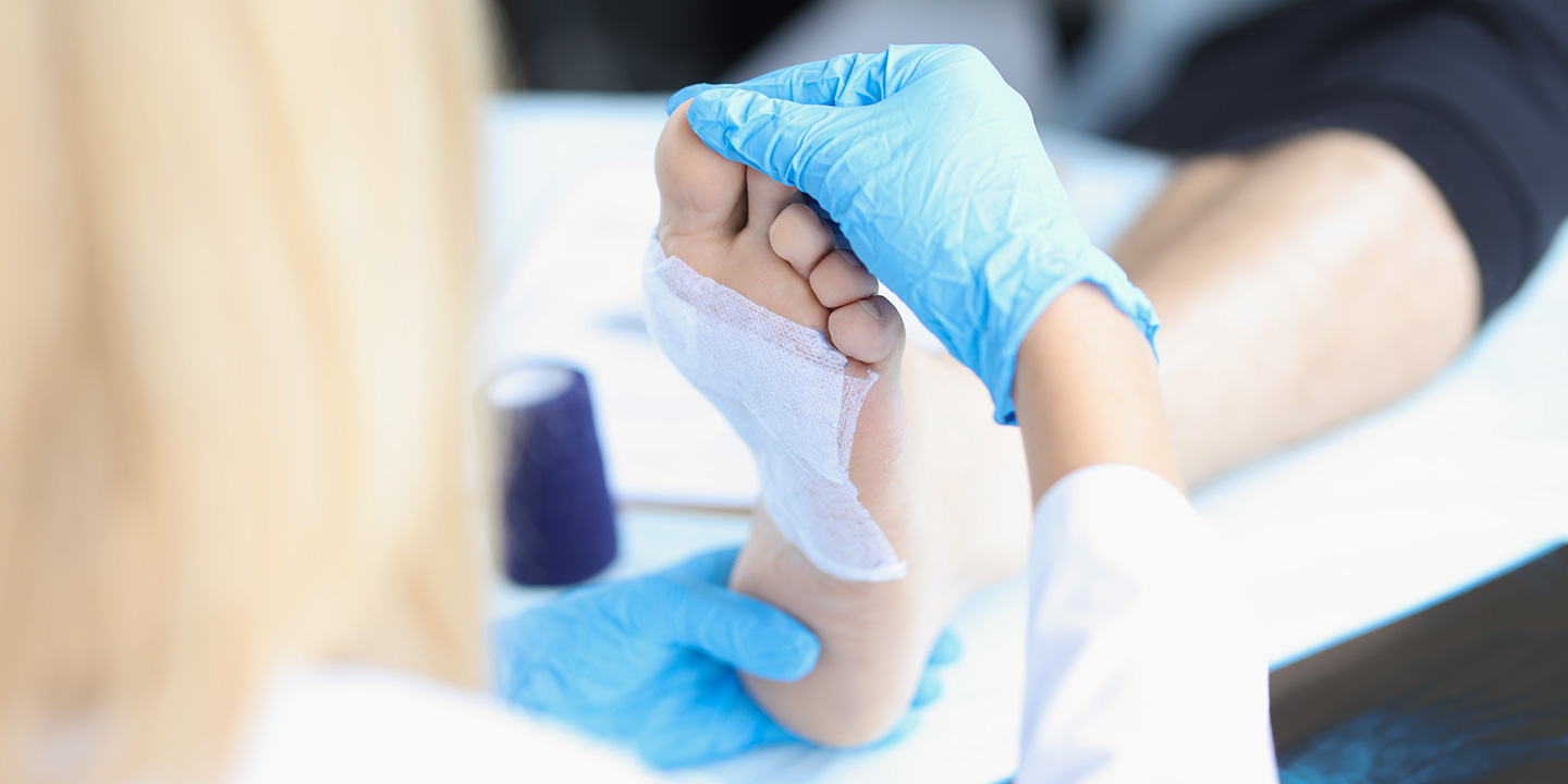 Zertifizierte Wundschwester der Medicus Wundambulanz in medizinischen Handschuhen untersucht Fuß eines Patienten
