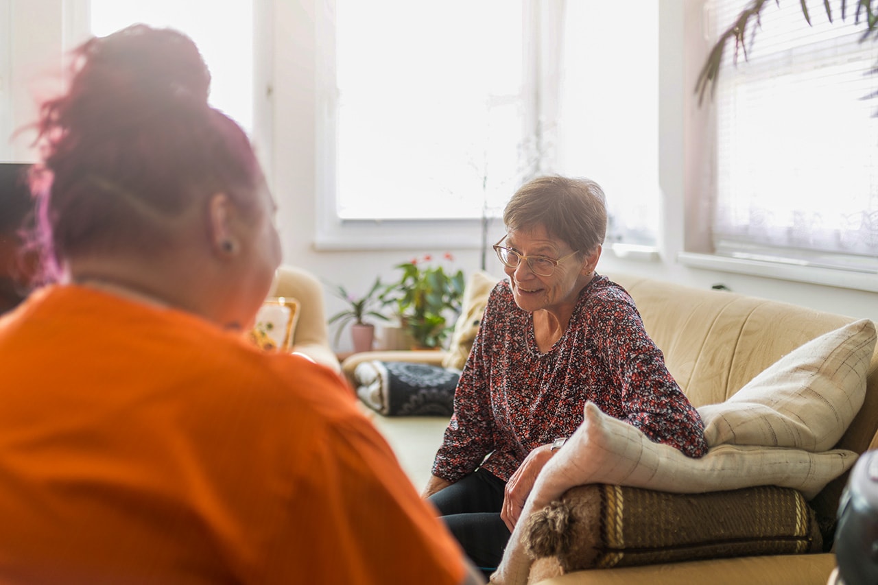 Bewohnerin in Ihrem Appartement und Pflegerin in orangenem Kasack im Gespräch