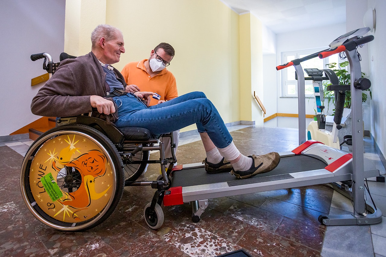 Senior im Rollstuhl mit Pfleger macht Fitnessübung auf Laufband